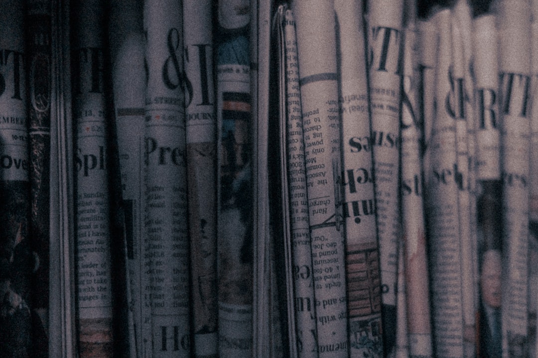 A row of newspapers stacked on a dark shelf